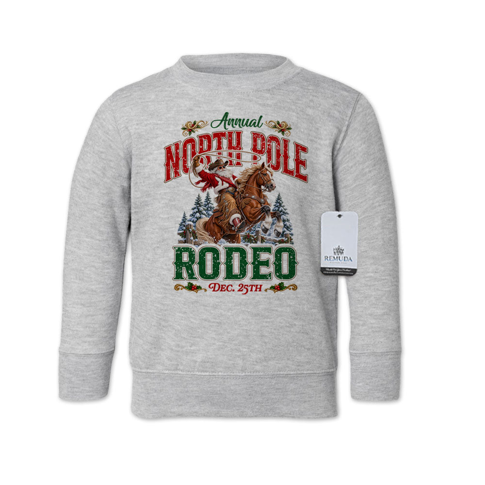 Heather Gray toddler crewneck fleece sweatshirt featuring a festive North Pole Rodeo Christmas design with Cowboy Santa riding a rearing horse, snowy pine trees, vintage red and green lettering, December 25th details, and ribbed cuffs and hem.