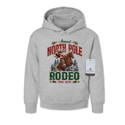 Heather Gray youth pullover fleece hoodie featuring a festive North Pole Rodeo Christmas design with Cowboy Santa riding a rearing horse, snowy pine trees, vintage red and green Western lettering, December 25th details, a front kangaroo pocket, and ribbed cuffs and hem.