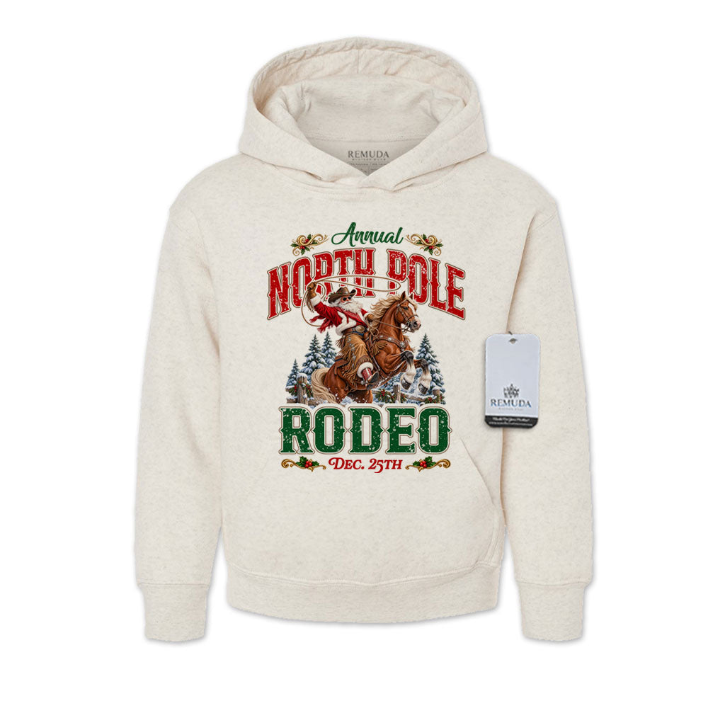 Oatmeal-colored youth pullover fleece hoodie featuring a festive North Pole Rodeo Christmas design with Cowboy Santa riding a rearing horse, snowy pine trees, vintage red and green Western lettering, December 25th details, a front kangaroo pocket, and ribbed cuffs and hem.
