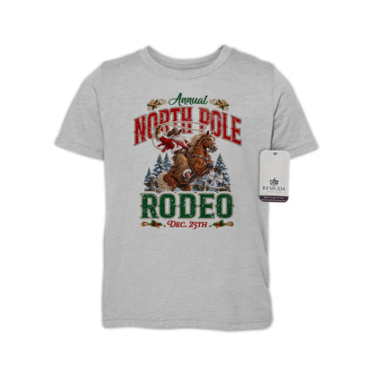 Heather Gray youth short sleeve T-shirt featuring a festive North Pole Rodeo Christmas design with Cowboy Santa riding a rearing horse, snowy pine trees, vintage red and green Western lettering, December 25th details, and a classic crewneck style.