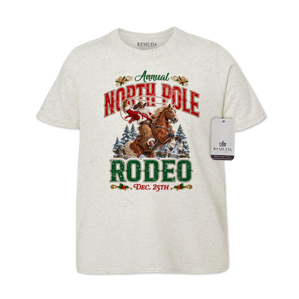 Oatmeal-colored youth short sleeve T-shirt featuring a festive North Pole Rodeo Christmas design with Cowboy Santa riding a rearing horse, snowy pine trees, vintage red and green Western lettering, December 25th details, and a classic crewneck style.
