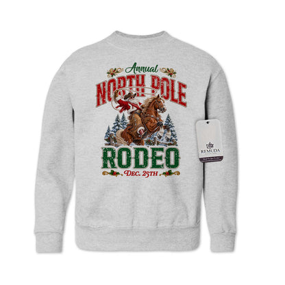 Ash gray youth crewneck fleece sweatshirt featuring a festive North Pole Rodeo Christmas design with Cowboy Santa riding a rearing horse, snowy pine trees, vintage red and green Western lettering, December 25th details, and ribbed cuffs and hem.