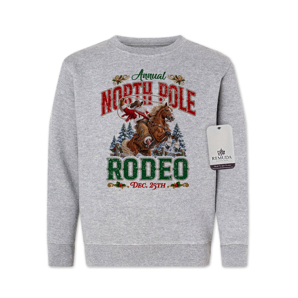 Heather gray youth crewneck fleece sweatshirt featuring a festive North Pole Rodeo Christmas design with Cowboy Santa riding a rearing horse, snowy pine trees, vintage red and green Western lettering, December 25th details, and ribbed cuffs and hem.