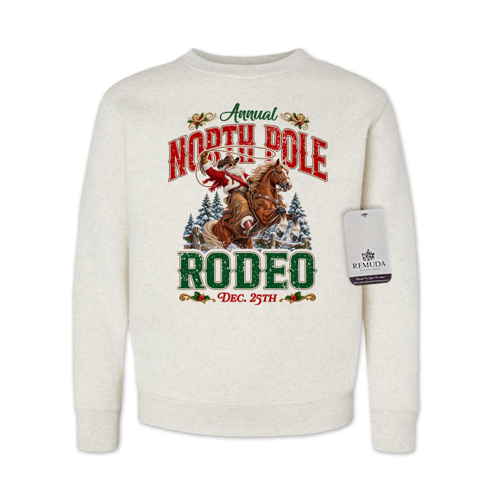 Oatmeal-colored youth crewneck fleece sweatshirt featuring a festive North Pole Rodeo Christmas design with Cowboy Santa riding a rearing horse, snowy pine trees, vintage red and green Western lettering, December 25th details, and ribbed cuffs and hem.