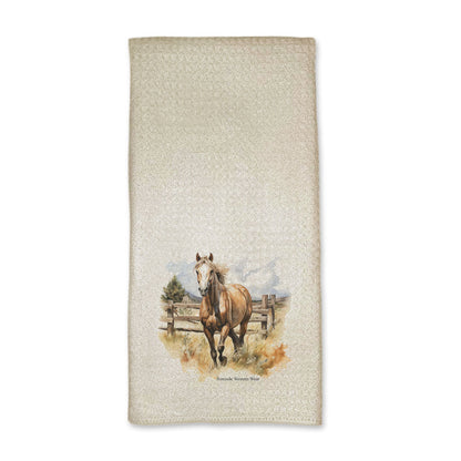 A vibrant western style kitchen hand towel featuring a beautiful palomino horse running in a field with a wooden fence behind him. Comes in a cream color. The design captures the spirit of western culture.