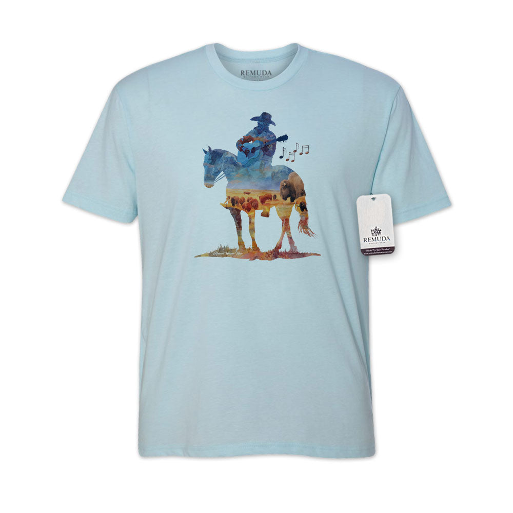 Watercolor-style illustration on a western light blue colored t-shirt showing a cowboy on horseback playing a guitar, with a soft, artistic western aesthetic titled “Where The Buffalo Roam.”