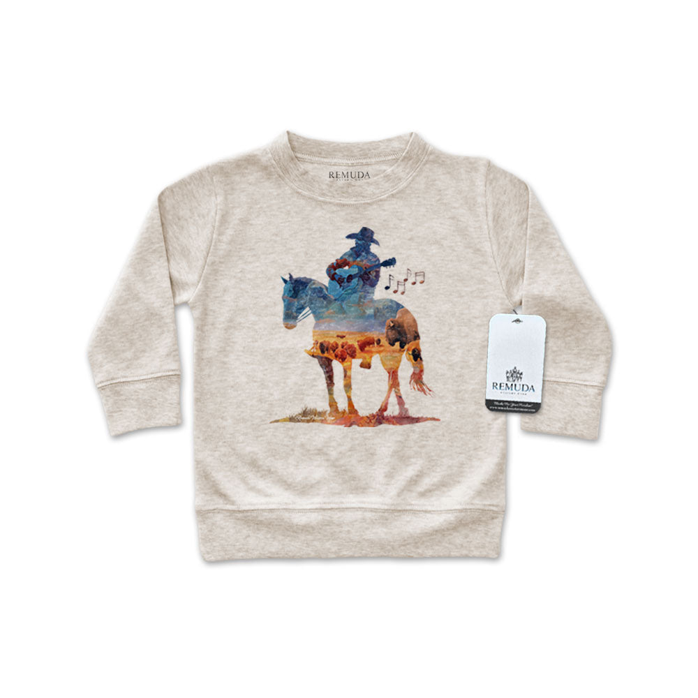 Watercolor-style illustration on an oatmeal colored infant long sleeve pullover showing a cowboy on horseback playing a guitar, titled “Where The Buffalo Roam,” in a soft, artistic western design.